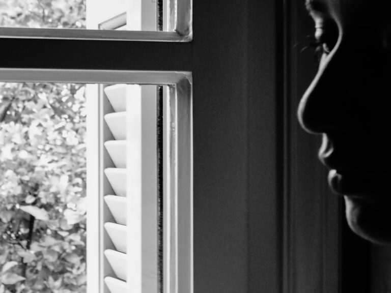 Πρόσωπο σε προφίλ στη σκιά, δίπλα σε παράθυρο με μισάνοιχτα παντζούρια.